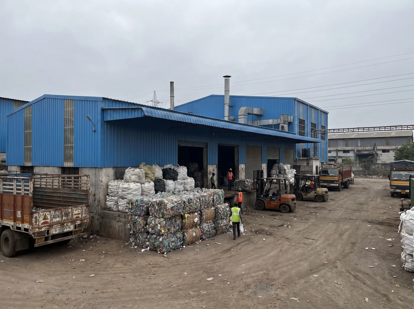 Exterior of a ZWL recycling unit with baled plastic, forklifts, and collection trucks in an Indian industrial estate